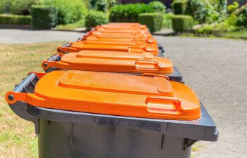 Row of plastic waste bins with orange lids.